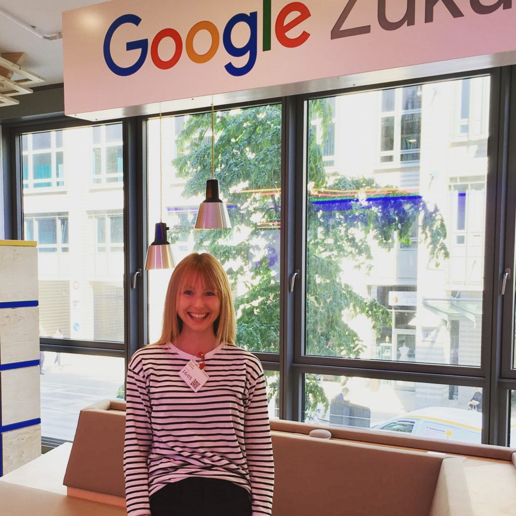 Ein blondes Mädchen steht unter dem Logo der Google Zukunftswerkstatt in Hamburg. Die Räumlichkeiten sind lichtdurchflutet und in den Farben (blau, rot, grün, gelb) des Google-Logos gestaltet.